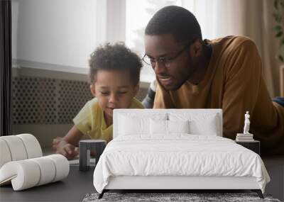 Happy black father and toddler son reading book at home Wall mural