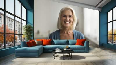 Happy blonde senior retired woman looking at camera with perfect toothy smile, posing at home, laughing. Cheerful positive pretty older lady head shot video call front portrait Wall mural