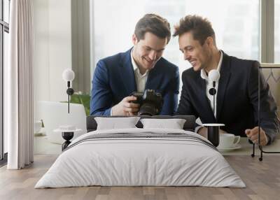 Happy businessman holding new professional camera, showing photographs to smiling colleague, partners viewing discussing pictures of business object, satisfied client looking at photos for project ads Wall mural