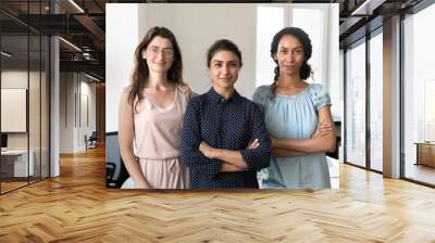 Happy confident beautiful diverse businesswomen standing together in office, looking at camera, smiling. Successful young business professionals women, leaders, colleagues front portrait Wall mural