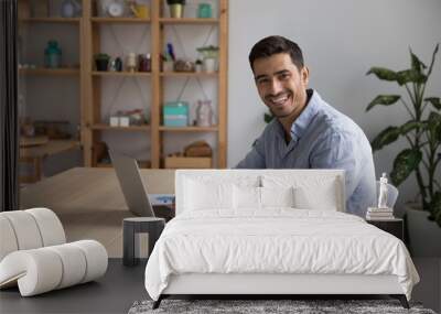 Happy confident businessman, entrepreneur, small business owner portrait at home office workplace. Young handsome freelance employee, student using laptop computer, looking at camera, smiling Wall mural