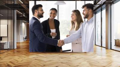 Happy confident diverse male business partners shaking hands at meeting, standing in office hall, closing deal, getting agreement, finishing successful work project with handshake Wall mural