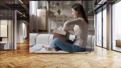 Happy curious impatient shopper opening carton box with purchase from internet shop, unwrapping package, holding paper container. Woman receiving parcel from order delivery service Wall mural