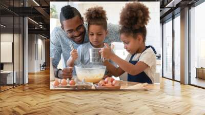 Happy dad teaching two cute preschooler kids to bake. Children and daddy beating eggs and sifting flour into bowl for kneading dough, making pie, cookies together. Family cooking, home bakery concept Wall mural