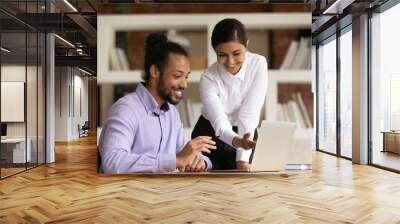 Happy diverse young multiracial businesspeople brainstorm work together on laptop in office. Smiling multiethnic colleagues coworkers look at computer screen cooperate. Teamwork concept. Wall mural