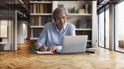 Happy elder student in headphones watching learning webinar on laptop, virtual workshop, writing notes. Getting knowledge, new profession, studying online from home, taking e-learning course Wall mural