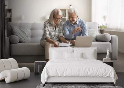 Happy elderly couple sit on couch, read paper letter, sorting out documents, enjoying paperwork, checking investment, reviewing insurance, mortgage or rental agreement with good terms and conditions Wall mural