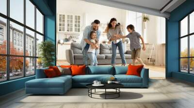 Happy family playing funny game having fun together with little son and daughter in modern living room. Young dad and mother with adorable cute children doing exercises, enjoying weekend at home. Wall mural