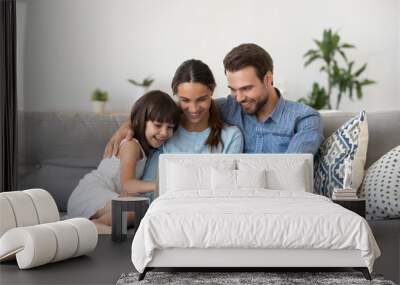 Happy family with kid girl having fun using laptop together sitting on sofa, parents and child daughter laughing relaxing at home with computer watching funny internet video, making online call Wall mural