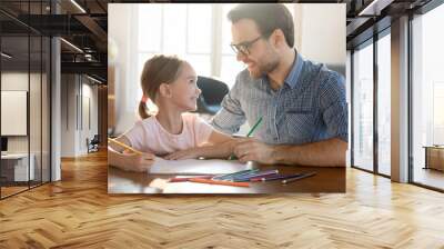 Happy father and adorable little daughter enjoying leisure time together close up, loving dad and preschool girl looking at each other, drawing colorful pencils in album, sitting at desk at home Wall mural