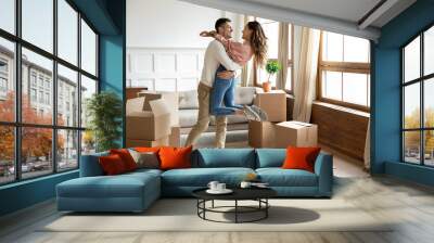 Happy husband lifting excited wife celebrating moving day with boxes Wall mural