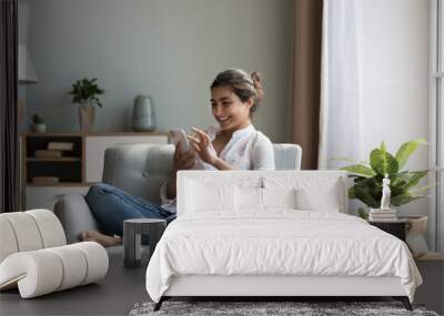 Happy Indian woman resting on cozy chair with smarthome, share messages to friend in social networks smile enjoy free time on internet. E-dating apps services for singles, electronic shopping at home Wall mural