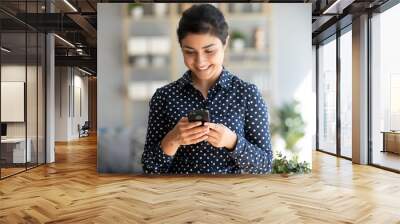 Happy indian young woman using mobile apps holding smart phone Wall mural