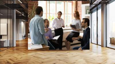 Happy inspired young mixed race colleagues discussing business ideas at brainstorming meeting in modern loft office. Friendly sincere motivated millennial multiracial employees developing project. Wall mural