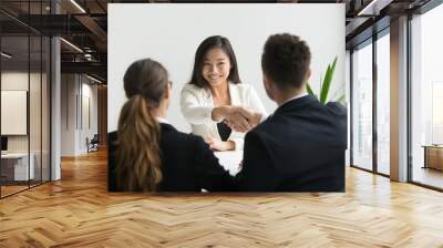 Happy millennial asian applicant getting hired shaking hand of hr, employer handshaking successful smiling chinese candidate congratulating with job interview win offering employment contract concept Wall mural