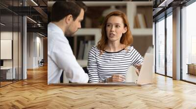 Happy millennial generation red haired woman discussing online project with skilled male leader in office. Motivated young diverse colleagues teammates working together, talking about problem solution Wall mural