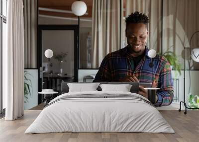 Happy millennial self employed professional using tablet in office. Young African American hipster guy, student, employee using virtual app, online service on pad computer, chatting, browsing Wall mural