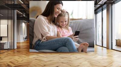 Happy mother and little daughter looking at phone screen together Wall mural