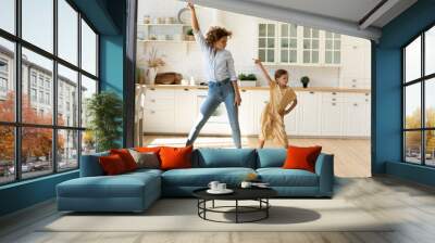 Happy mother and little daughter moving to favorite music in modern kitchen together, young mom teaching adorable kid girl to dance, family engaged in funny activity at home, enjoying leisure time Wall mural