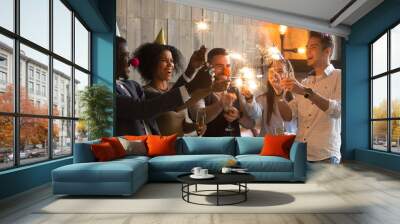 Happy multiracial people in party hats clown noses holding sparklers and champagne glasses celebrating New year eve together, excited diverse young friends having fun enjoying celebration together Wall mural