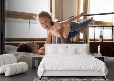 Happy mum lifting cute child daughter playing plane on bed Wall mural