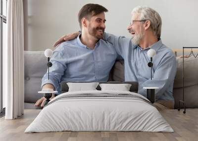 Happy old dad embracing young son talking laughing on sofa Wall mural