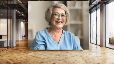 Happy positive blonde elder woman in stylish eyeglasses looking at camera with perfect toothy smile, laughing, posing for home portrait. Beautiful mature lady video call screen head shot Wall mural