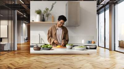 Happy pretty Black girl enjoying cooking hobby, chopping fresh vegetables for salad at kitchen table, making healthy dinner from organic bio ingredients, keeping vitamin rich nutrition Wall mural