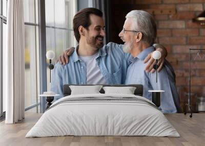 Happy senior 70s father and grown son sharing good news, talking and hugging at home, approving, encouraging, congratulating each other, giving support. Two generations, fatherhood, family relations Wall mural