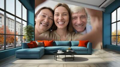 Happy senior parents and adult child woman portrait shot in hand heart shaped frame. Cheerful elder mom, dad, daughter having fun, posing together, looking at camera, laughing, smiling Wall mural