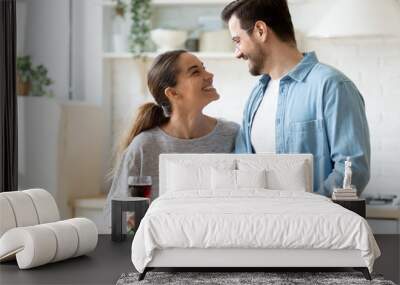 Happy young couple cooking dinner in kitchen at home together, smiling husband cutting fresh vegetables, preparing salad, beautiful wife holding wine glass, enjoying romantic moment, having fun Wall mural