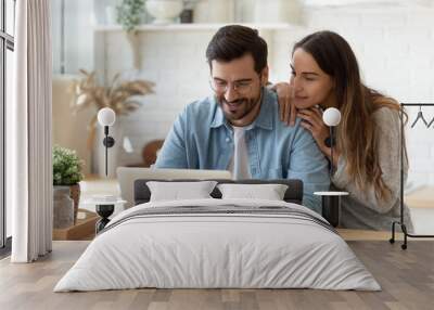 Happy young man and woman hugging, using laptop together, looking at screen, loving couple shopping or chatting online, using internet banking services, reading news in social network Wall mural