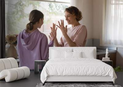 Happy young mom and teenage daughter having fun dancing in kitchen. Smiling mommy teaching teen kid girl to wash showing clean hands before cooking or eating enjoying family life together at home. Wall mural