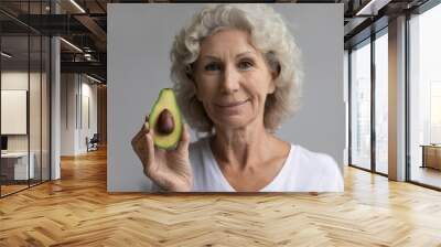 Head shot portrait beautiful middle aged woman holding avocado, looking at camera, attractive mature senior female recommending healthy lifestyle, natural organic cosmetics product, diet Wall mural