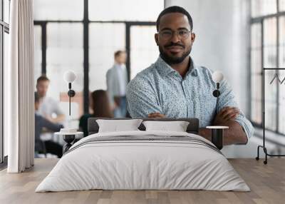 Head shot portrait confident young African American businessman wearing glasses looking at camera, successful executive startup founder standing in modern office room with arms crossed Wall mural