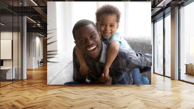 Head shot portrait happy smiling African American family, smiling father and piggyback little preschooler son, man holding small boy on back, embracing, hugging, sitting together, looking at camera Wall mural