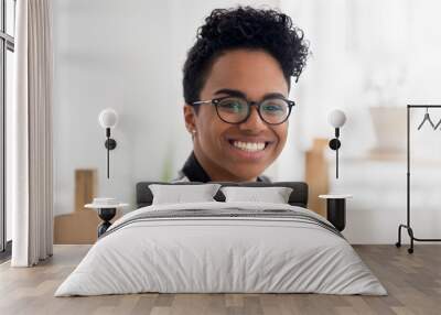 Head shot portrait of millennial african female sitting at the desk in office room looking at camera smiling. Close up of student or businesswoman with eyeglasses indoors. Success, leadership concept Wall mural