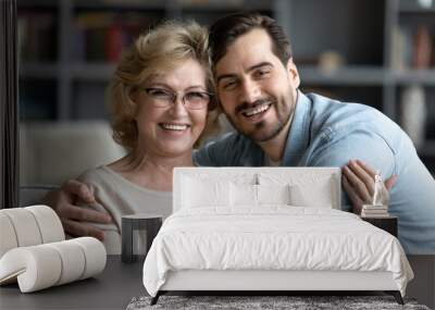 Head shot portrait of smiling young caucasian man embracing affectionate older senior mother in glasses, enjoying sweet tender time indoor, spending weekend leisure together, family relations concept. Wall mural