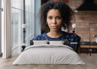 Head shot portrait of young serious african american woman standing in own apartment. Beautiful millennial mixed race lady looking at camera, feeling thoughtful alone at home, posing for photo. Wall mural