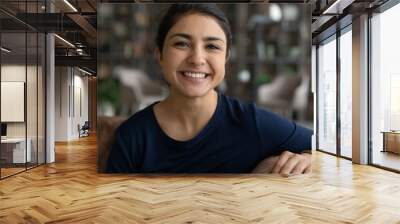 Head shot portrait smiling attractive Indian woman making video call, sitting on couch at home, happy young female chatting online with friends or relatives, internet meeting, blogger recording vlog Wall mural