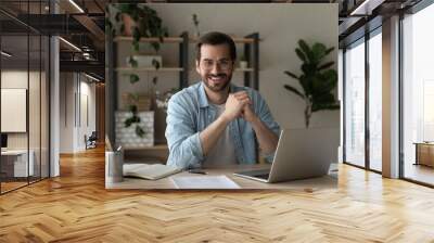 Head shot portrait smiling confident businessman wearing glasses sitting at table with laptop and documents, looking at camera, successful happy entrepreneur or student posing at workplace Wall mural