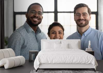 Head shot portrait smiling successful diverse employees team standing in modern office, happy overjoyed Indian businesswoman, African American and Caucasian businessmen looking at camera Wall mural