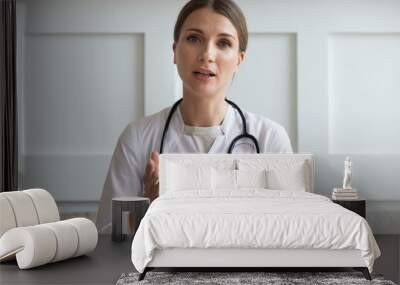 Head shot portrait woman doctor talking online with patient, making video call, looking at camera, young female wearing white uniform with stethoscope speaking, consulting and therapy concept Wall mural