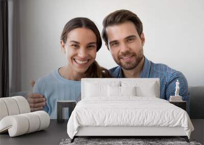 Headshot portrait of happy smiling millennial couple sitting on sofa at home embracing looking at camera, young man and woman making video call communicating online or recording vlog together Wall mural