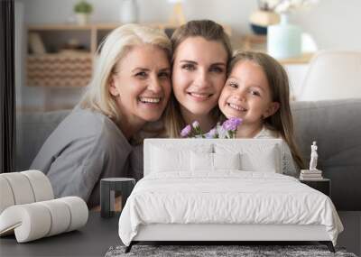 Headshot portrait of happy three generations women family celebrating mothers day birthday together, smiling grandmother and kid daughter congratulating young mom with flowers gift looking at camera Wall mural