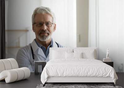 Headshot portrait of serious mature male doctor or therapist in white medical uniform, glasses and stethoscope, mature old man GP or physician in spectacles pose at workplace, healthcare concept Wall mural