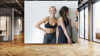 Horizontal image cheerful girls wearing activewear standing holding yoga mats Wall mural