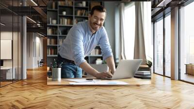 In modern office good-looking businessman young entrepreneur successful business owner standing leaned over workplace desk smile look at camera feels confident. Freelancer or teacher portrait concept Wall mural