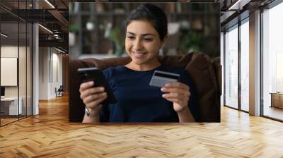 In one touch. Smiling young mixed race female client use prepaid plastic card and phone web app to book tickets online make room reservation at hotel abroad. Indian woman check ebank account by phone Wall mural