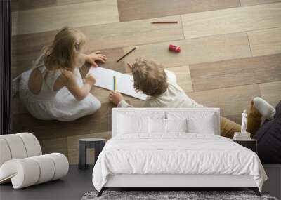 Kids sister and brother playing drawing together on wooden warm floor in living room, creative children boy and girl having fun at home, siblings friendship, underfloor heating concept, top view Wall mural